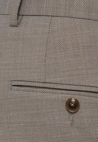 Γκρι υφασμάτινη υφή με σφιχτό ύφανση. Περιλαμβάνει ένα ορατό κουμπί και μία τσέπη με πατούρα κατά μήκος της ραφής. Διακριτό χρωματικό σχέδιο.