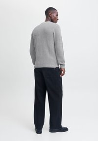 Pull en maille côtelée gris avec des manches longues, associé à un pantalon large noir. Texture lisse et coupe décontractée, avec un design simple.