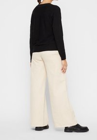 Pull noir à manches longues associé à un pantalon large crème et des chaussures noires, mettant en avant une silhouette simple et décontractée.