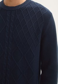 Pull marin avec des motifs de tricot texturés, mettant en avant des formes de diamant et un motif en câble. Col côtelé et texture douce.