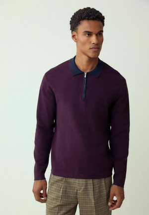 Dunkellila Pullover mit Reißverschluss, kontrastierendem marineblauem Kragen mit roter Naht, Strickstruktur und langen Ärmeln.