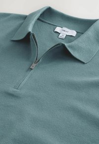 Herre zip-up polo i tekstureret, akvagrøn stof. Har en krave og en sølv lynlås. Etiketten viser "NEXT" med størrelse M.
