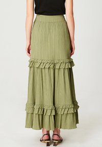 Jupe maxi dégradée et froncée en tissu olive doux, avec une surface texturée et une large ceinture. Associée à un haut noir et des sandales.