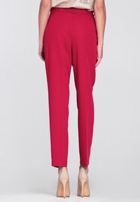 Czerwone dopasowane spodnie z wysokim stanem i zwężanymi nogawkami, o gładkiej fakturze i kieszeniach, zestawione z cielistymi szpilkami.