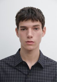 Donker geruit overhemd met een button-down kraag en knopen op de borst. De stof heeft een gladde textuur met contrasterende lichte lijnen in het patroon.