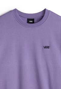 Sudadera de algodón morada con cuello redondo que presenta un pequeño logo negro de Vans en el lado izquierdo del pecho y con cuellos y puños de canalé. Textura suave.