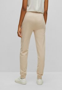 Beige Jogginghose aus weichem Stoff, mit taperndem Schnitt, elastischem Bund und gerippten Bündchen. Kombiniert mit weißen Sneakern.