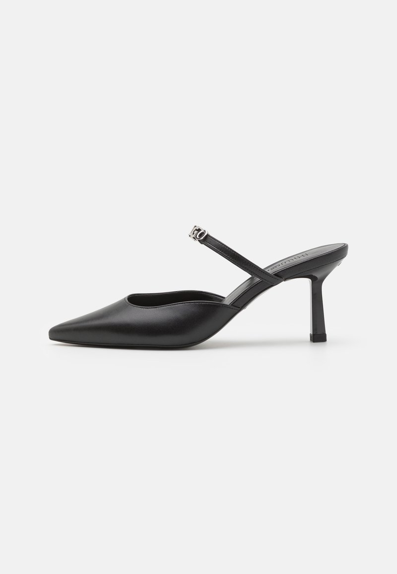 Mule en cuir noir avec un bout pointu et un talon fin. Dotée d'une fine bride avec une pièce métallique. Texture lisse, design minimaliste.