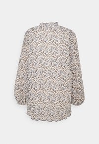 Blouse à manches longues, ample, avec un petit imprimé floral noir et bleu sur tissu blanc, dotée d'un col montant froufroutant et d'un ourlet festonné.