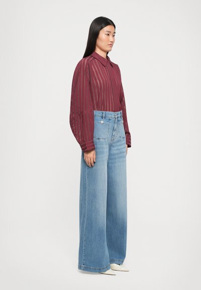 Burgunderrandede langermede skjorte med krage, sammen med vide lyseblå jeans. Glatt stoff og avslappet passform.