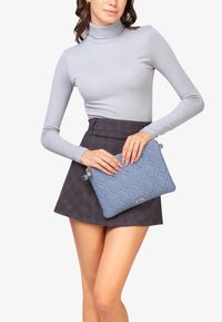 Bolso acolchado azul con un acabado suave; presenta un acento de hardware plateado y el nombre de la marca "V73" grabado en la esquina inferior derecha.