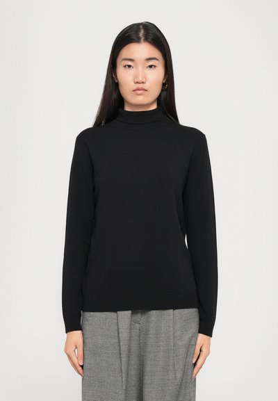 Suéter negro de manga larga con cuello alto en un material suave, con una silueta ajustada y puños acanalados, combinado con pantalones de cuadros grises.