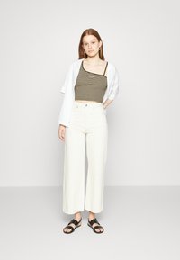 Top de alças finas listrado em castanho e creme, combinado com calças largas brancas de cintura alta e sandálias pretas. Design minimalista geral.