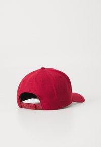 Casquette de baseball rouge en tissu texturé, avec une visière courbée et une fermeture à pression réglable à l'arrière. Design simple sans logos visibles.