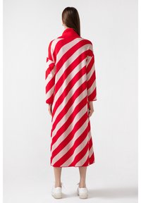 Cardigan long rayé rouge et beige avec un col haut et des manches longues, présenté de dos. Le matériau semble doux et texturé.