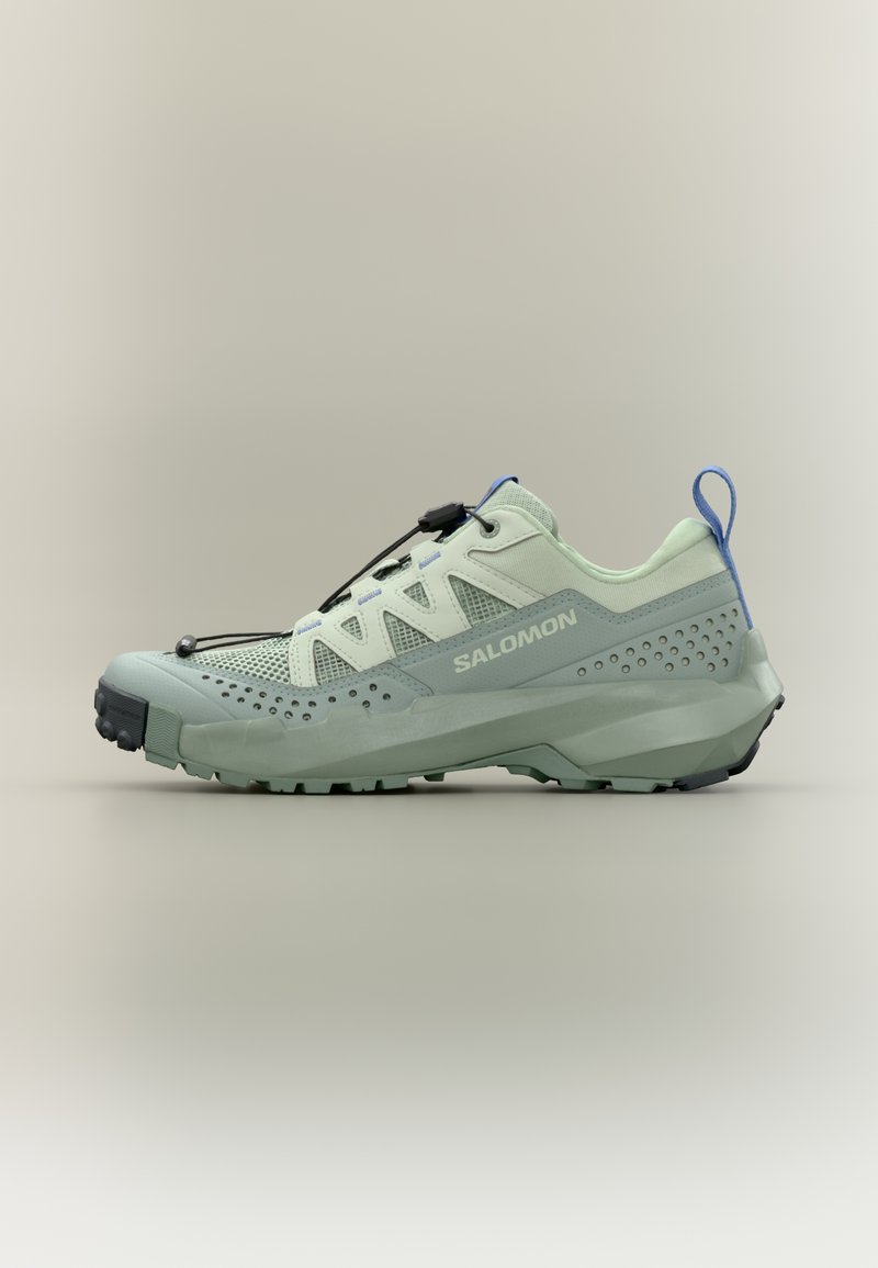 Lichtgroene en grijze Salomon trailrunningschoen met geperforeerde zijkanten, mesh bovenwerk, snel vetersysteem en blauwe trekstrip bij de hiel.