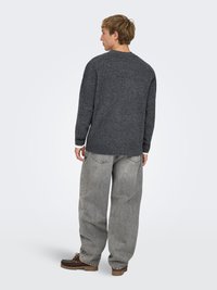 Charcoal gray sweater with a relaxed fit and ribbed cuffs; paired with loose light gray jeans and brown footwear. Basic round neckline.