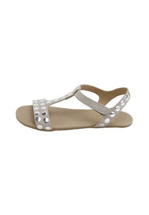 Sandalia plana beige con tira en T y correa en el tobillo, decorada con tachuelas redondas reflectantes plateadas.