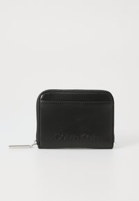 Melnas ādas maku ar rāvējslēdzēja aizdari. Priekšpusē ir reljefā "Calvin Klein" logo. Gluda tekstūra un taisnstūrveida forma.