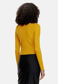 Maglione giallo a coste con maniche lunghe, design aderente e scollatura rotonda, abbinato a una gonna nera elegante.