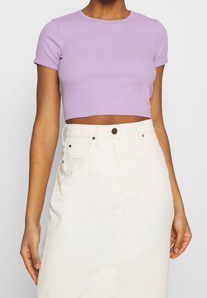 Lila gerippter Cropped-Top mit kurzen Ärmeln und einem gewellten Ausschnitt, kombiniert mit einem hochtaillierten cremefarbenen Rock mit vorderen Knöpfen.
