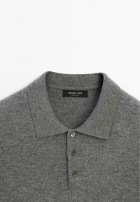 Polo grigio realizzato in tessuto a maglia, con colletto classico, tre bottoni e un'etichetta che reca la scritta "Massimo Dutti."