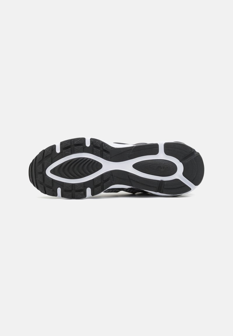 Suela de zapatilla deportiva negra con un patrón de agarre de goma texturizada, acentos en blanco y un diseño curvado. Presenta surcos profundos para mayor tracción.