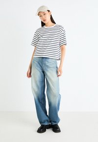 Striped white and navy t-shirt paired with light blue wide-leg jeans and black shoes, complemented by a beige baseball cap.