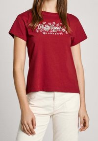 Röd bomullströja med korta ärmar, med en blommönstring och "Pepe Jeans London"-text i vitt i mitten.