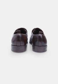 Chaussures en cuir marron avec une finition lisse, bout arrondi et talon empilé. Présente une couture subtile le long de l'arrière et une boucle pour un enfilage facile.