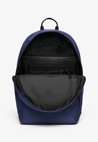 Mochila azul marino con forma redondeada y abertura con cremallera. En su interior cuenta con un forro negro y un bolsillo de malla para organización.