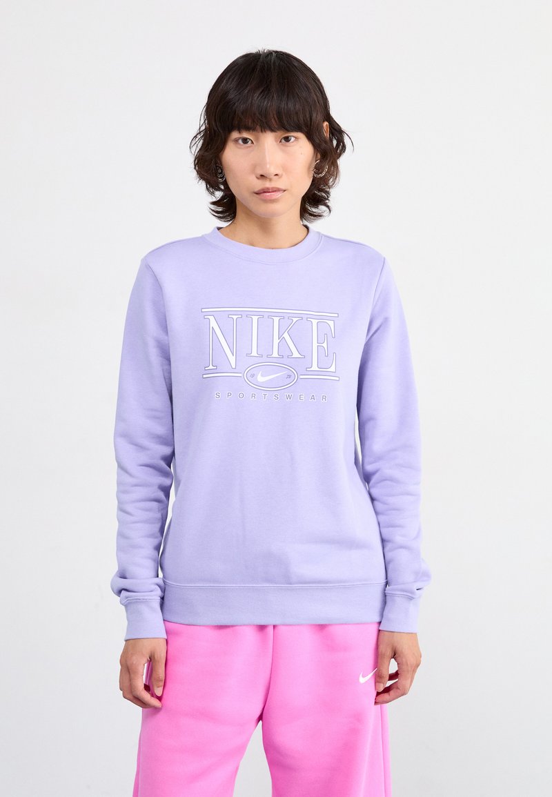 Sweat-shirt violet clair avec des poignets et un ourlet côtelés, arborant un logo blanc "NIKE SPORTSWEAR" sur le devant. Matière en mélange de coton lisse.