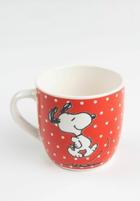Red ceramic mug with white polka dots, featuring a cartoon dog design in black and white. Smooth surface and curved handle.