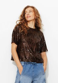 Haut marron à sequins avec manches courtes et encolure ronde, associé à un short en denim bleu clair avec taille à cordon et poches.