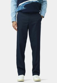 Navyblaue Hose aus weichem Material, mit entspanntem Schnitt und geradem Bein. Getragen mit weißen Sneakern, maßgeschneiderter Gestaltung und minimaler Detailierung.