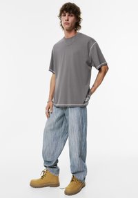 Grå oversized t-shirt med kontraststing, parret med lyseblå vide jeans og gule snørebåndsstøvler. Minimalistisk design.