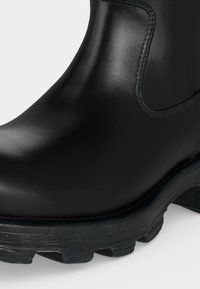 Bottine en cuir noir avec panneau latéral élastique et semelle épaisse texturée pour l’adhérence, vue en gros plan.