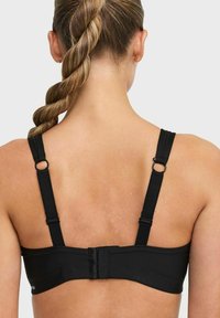 Svart bh med justerbara remmar och hårdvaruaccents, samt en jämn textur. Flera hyschar bak för en säker passform.