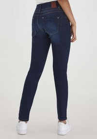 Sötétkék farmer skinny farmer, magas derekú, sima textúrával. Hátsó zsebek varrása és barna bőr címke a derékpánton.