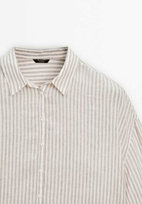 Chemise à rayures verticales beige et blanc avec boutons et col, présentée sur un fond blanc, montrant le haut du devant et l'épaule.