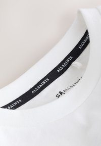 Col rond de t-shirt blanc avec une bande d’étiquette intérieure noire affichant le texte répété "ALLSAINTS" en blanc.