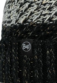 Gorro de punto negro con acentos en blanco y beige, que presenta un patrón texturizado y una etiqueta negra con marca y logo en blanco.