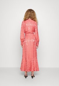 Långärmad korallblommig klänning med cinchad midja, utsvängd kjol, texturerad tyg och en volangsläpp. Svarta klacksandaler kompletterar looken.