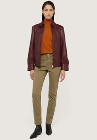 Burgunderfärgad läderjacka med krage, matchad med en orange polokrage och olivgröna byxor. Svarta ankle boots fulländar looken.