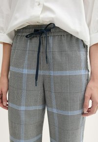 Geruite broek in grijs, zwart en lichtblauw; elastische tailleband met koord; zachte stof met een gestructureerd patroon en zijzakken.