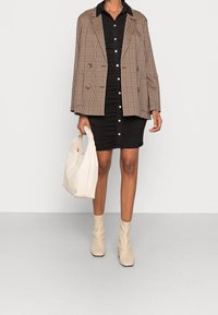 Blazer à carreaux marron, robe chemise noire à boutons, sac beige et bottines beiges décontractées. La tenue présente des textures variées et des détails à boutons.