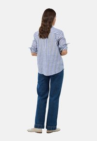 Chemise rayée bleue et blanche avec les manches retroussées, associée à un jean en denim bleu taille haute et des mocassins beiges, vue de dos.