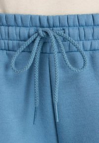Light blue sweatpants with a ribbed waistband, drawstring closure, and braided texture. Features two smooth, rounded tips on the drawstring.