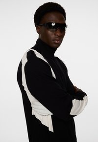 Svart polotröja med vita zickzack-accenter på ärmarna, med en slank design och en figurnära silhuett.