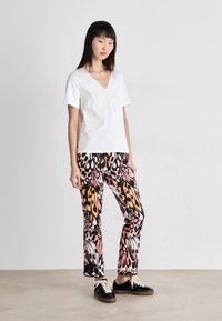 Witte korte mouwen V-hals top met gestructureerde borduursels; strakke broek met gedurfde, kleurrijke vlinder- en dierenprint; zwarte schoenen.